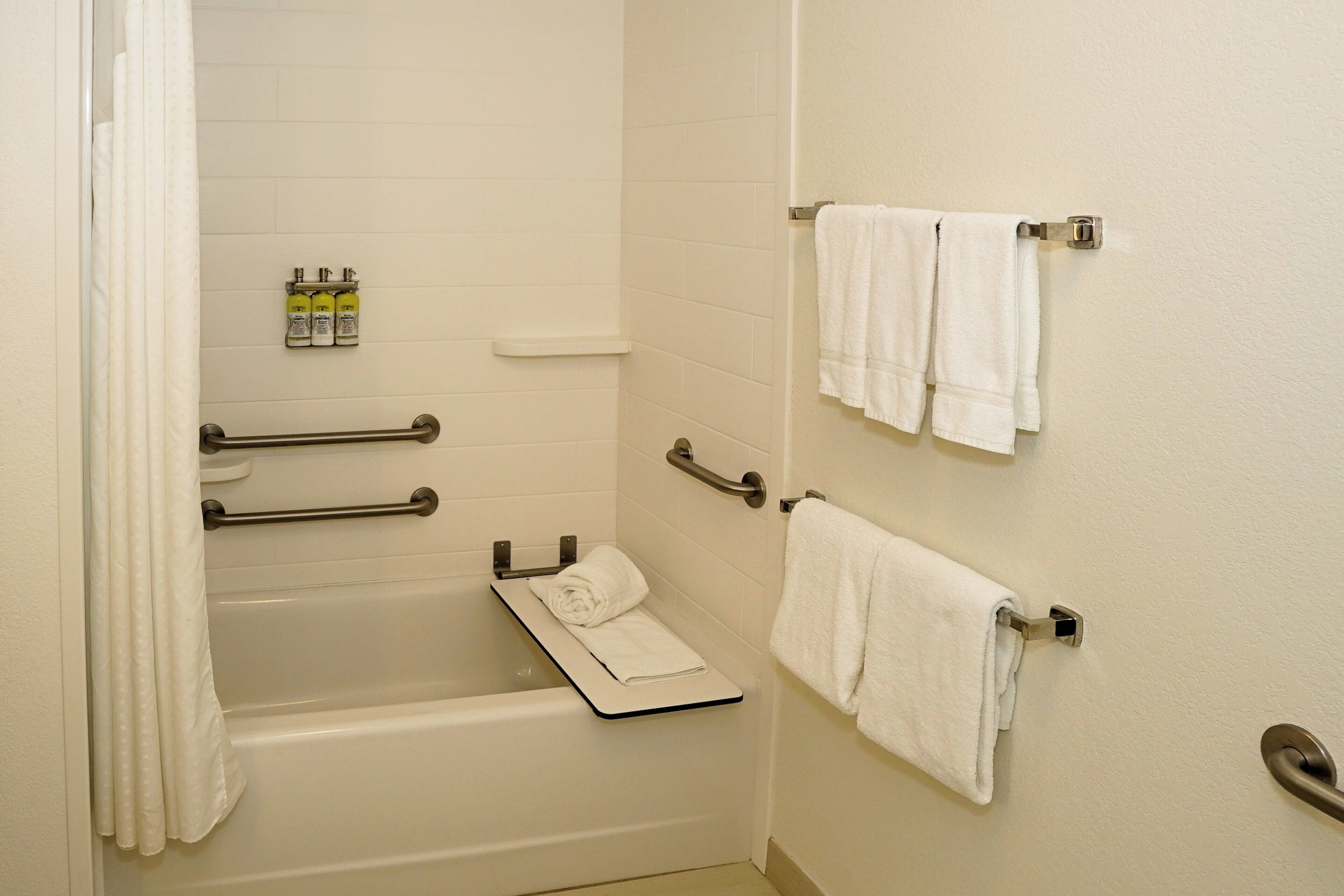 A bathroom with a bathtub, grab bars, a towel rack, and a shelf with toiletries.