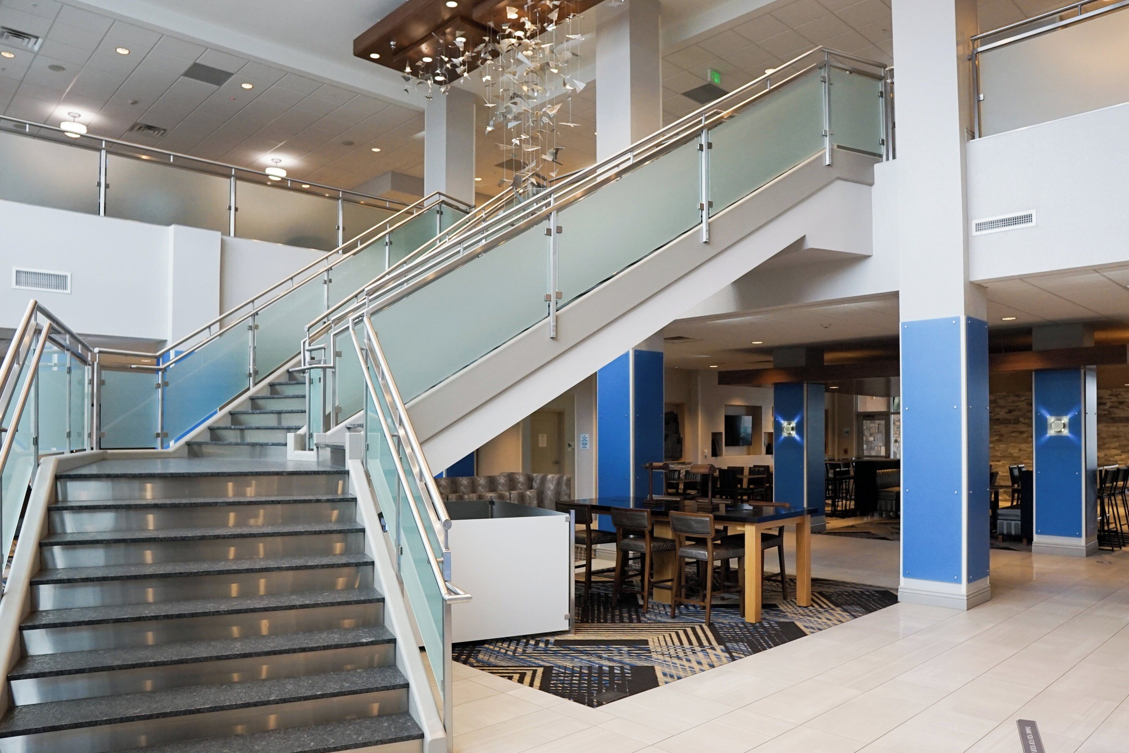 Un hall d’hôtel moderne avec un escalier en verre, un espace salon et un comptoir d’accueil.