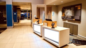A hotel reception area with two reception desks, a digital check-in kiosk, and a wall-mounted information board. - Holiday Inn Express & Suites Denver - Aurora Medical Campus by IHG (Aurora)