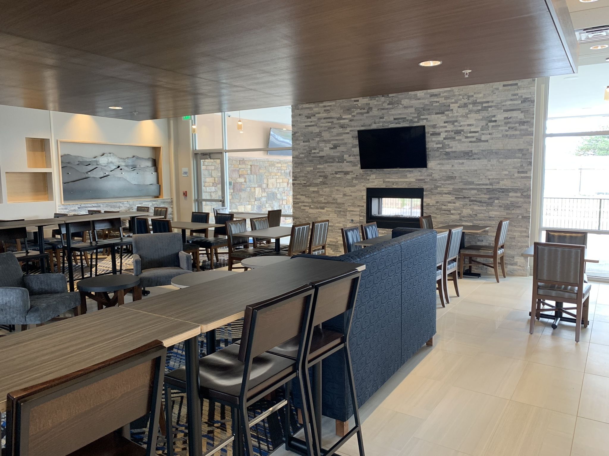 Un restaurante moderno con pared de piedra, televisor de pantalla plana y una variedad de opciones de asientos, incluyendo mesas y cabinas.