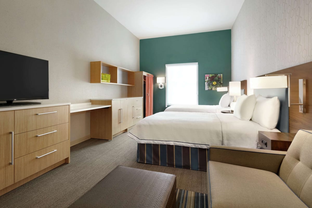 A modern hotel room with a bed, a television, a desk, and a wardrobe.