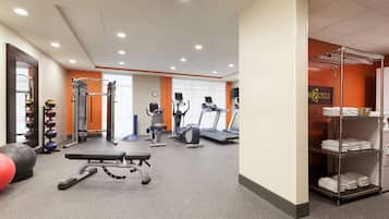 A gym with exercise equipment, a bench, and a rack of towels.