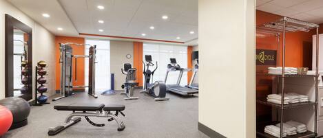 A gym with exercise equipment, a bench, and a rack of towels.