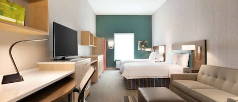 A modern hotel room with a desk, computer, flat-screen TV, bed, and seating area.