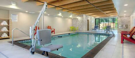 An indoor swimming pool with a lifeguard chair, a ladder, and a poolside area with chairs.