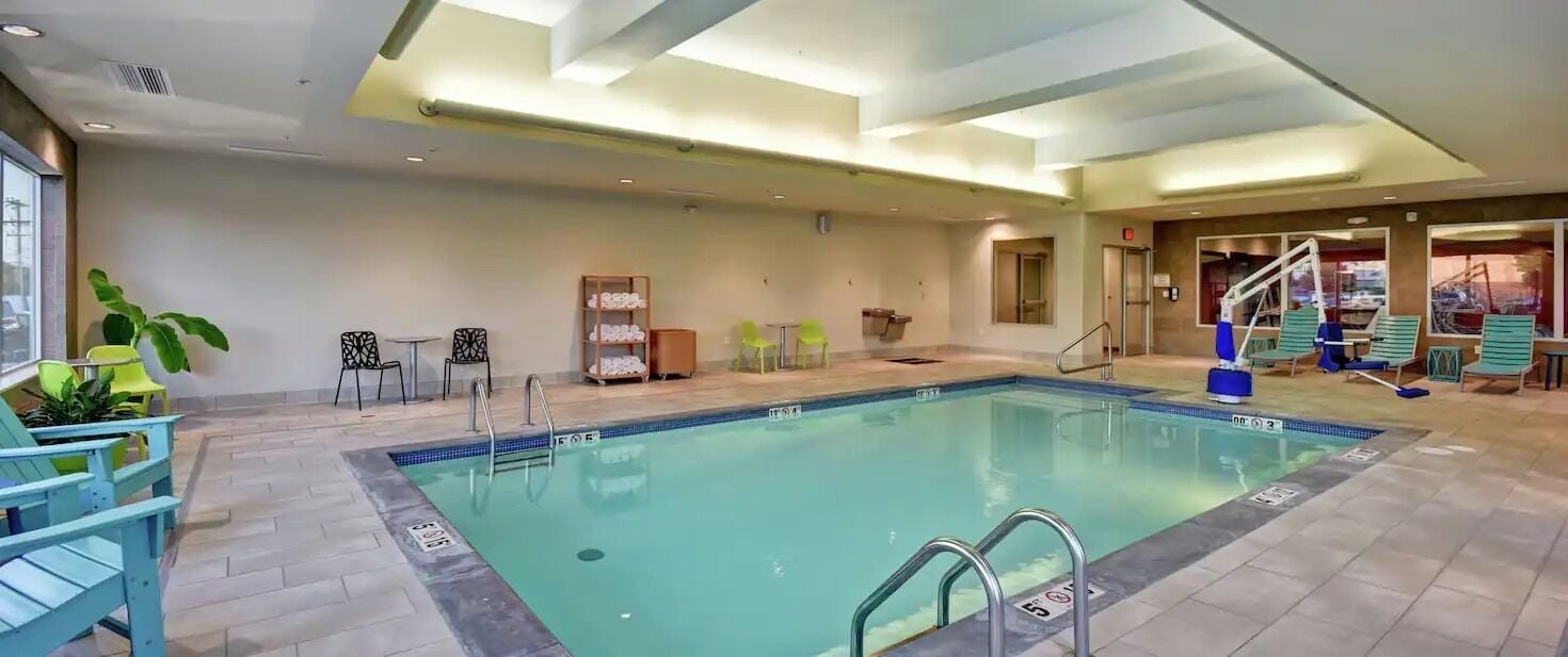 An indoor swimming pool with a tiled floor, surrounded by lounge chairs and a small seating area with tables.