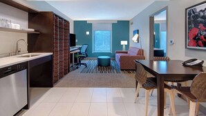 Una habitación de hotel moderna con cocina, una mesa de comedor con sillas, un sofá, un televisor y un ventanal grande.