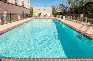A rectangular swimming pool with a brick border, surrounded by lounge chairs and umbrellas, and a brick building in the background. - Hampton Inn Opelousas (Opelousas)