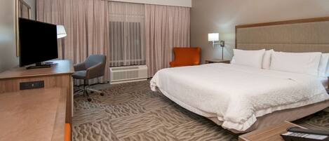 A hotel room with a bed, a desk, a chair, a television, and a window with curtains.