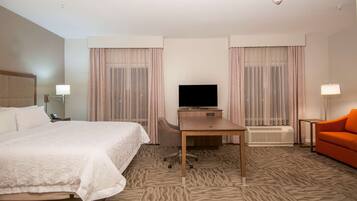 A hotel room with a bed, a desk, a television, a chair, and an orange sofa.