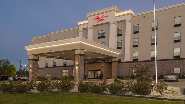 A Hampton Inn hotel with a clear entrance, a flagpole with the American flag, and a parking area.