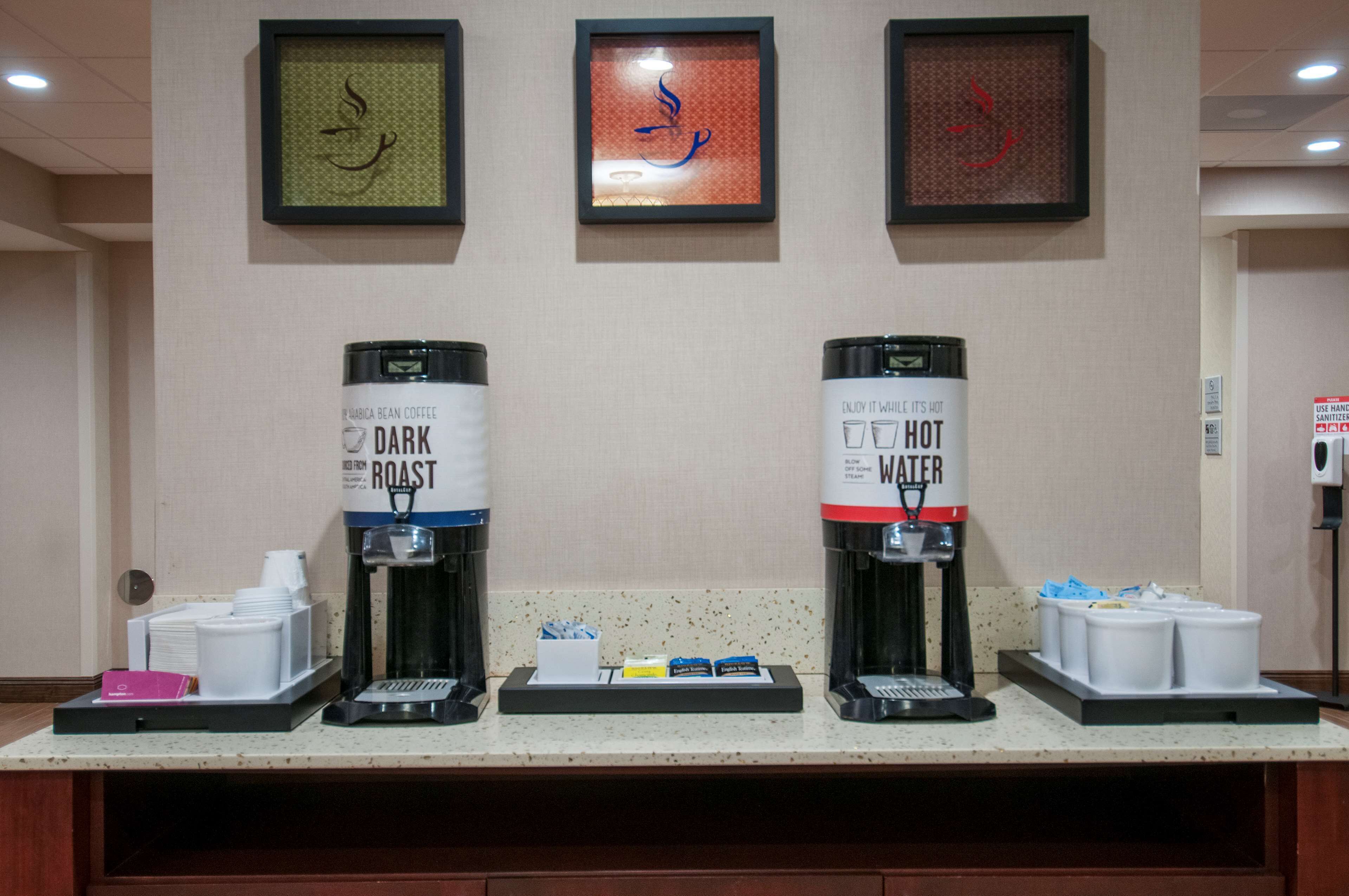 A coffee station with two coffee dispensers labeled "DARK ROAST" and "HOT WATER," and a tray with coffee cups and a tissue box.