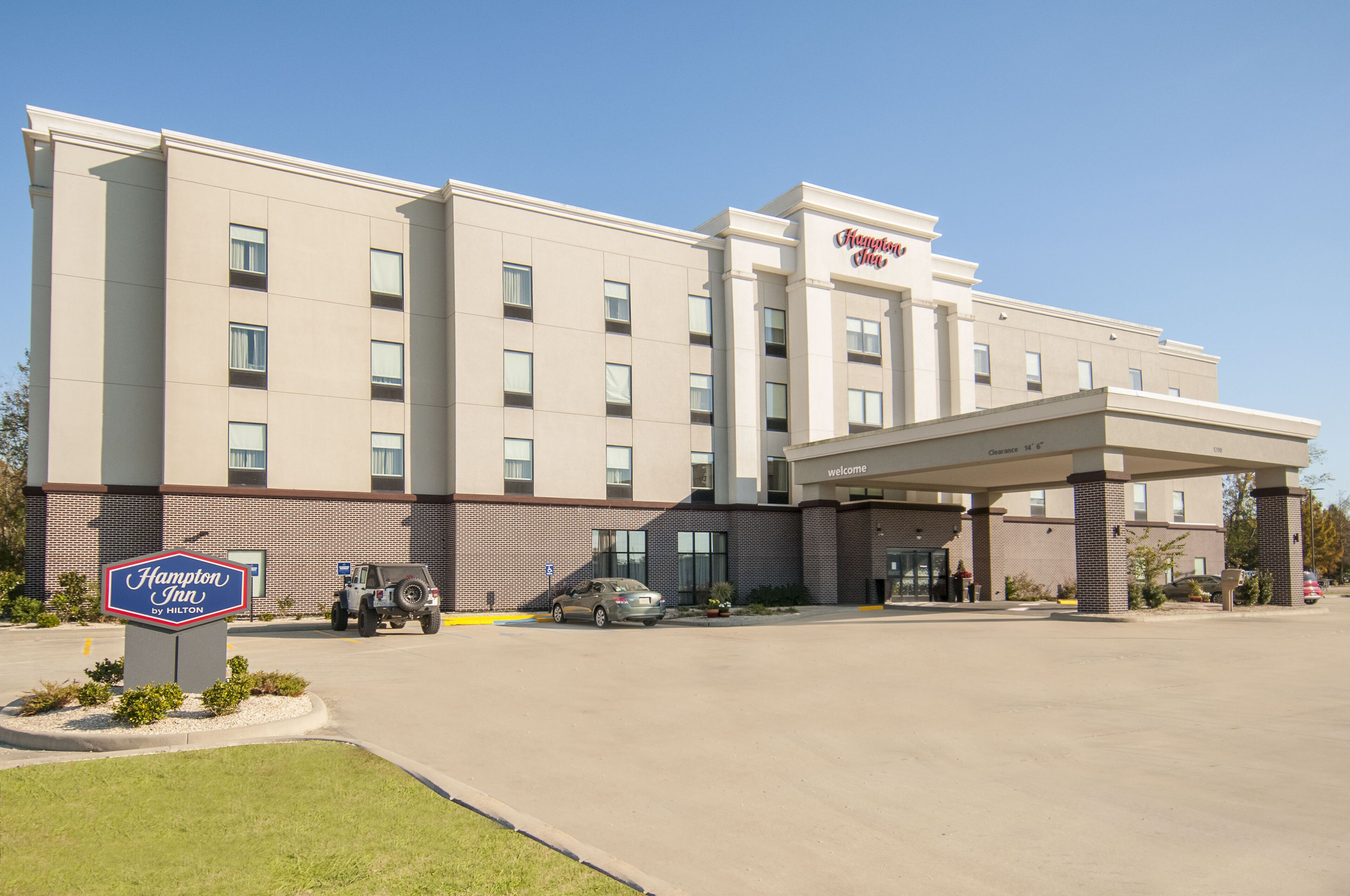 Un hotel Hampton Inn by Hilton con entrada techada, aparcamiento y un letrero con el nombre del hotel.