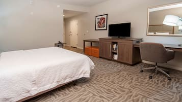 Ein Hotelzimmer mit Bett, Schreibtisch, Stuhl, Fernseher und Spiegel.