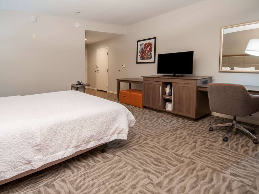 Ein Hotelzimmer mit Bett, Schreibtisch, Stuhl, Fernseher und Spiegel.