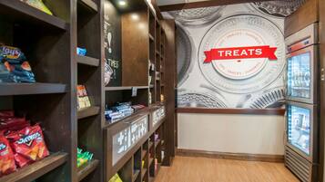 A snack display area with shelves stocked with various chips and snacks, a wall with a 'Treats' sign, and a refrigerated display case.