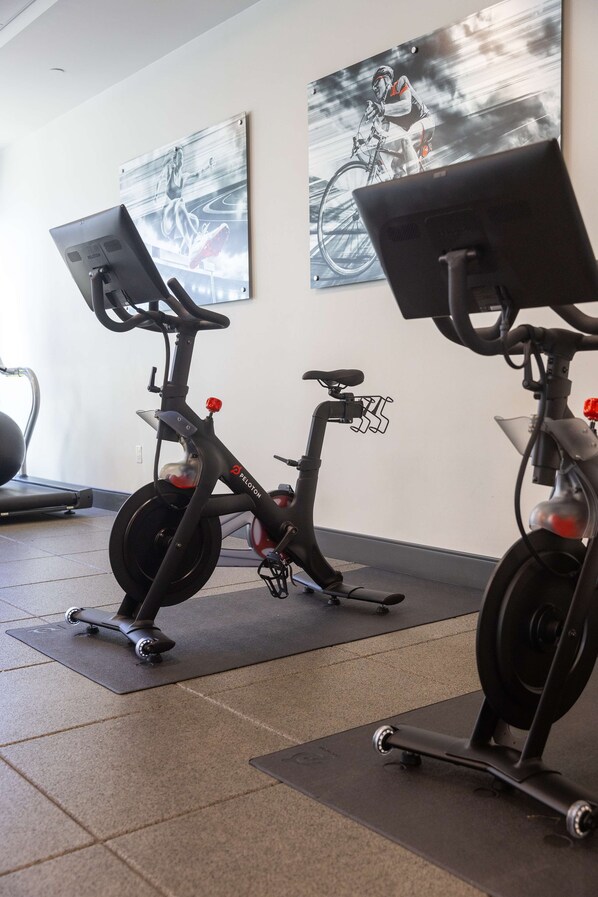 Une salle de sport équipée de vélos d’appartement, d’un tapis de course et de tapis de sol pour les exercices.