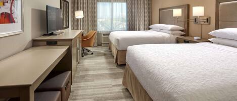 A hotel room with two beds, a desk, a chair, a TV, and a window with curtains.