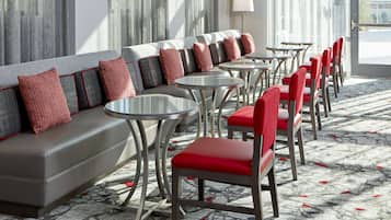 Un hall de hotel con un sofá, sillas rojas y mesitas.