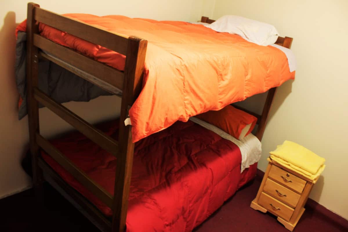 A bunk bed with orange bedding, a wooden nightstand with drawers, and a red carpeted floor.