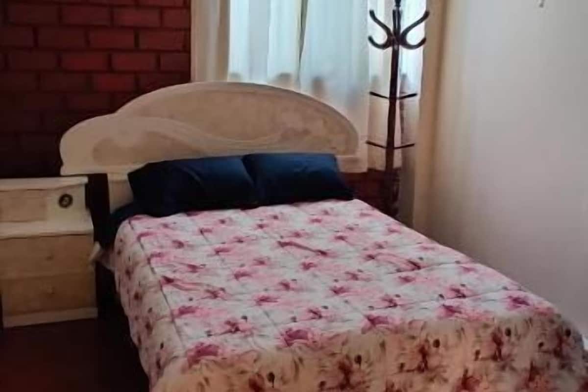 A bedroom with a bed, a nightstand, a coat rack, and a window with curtains.