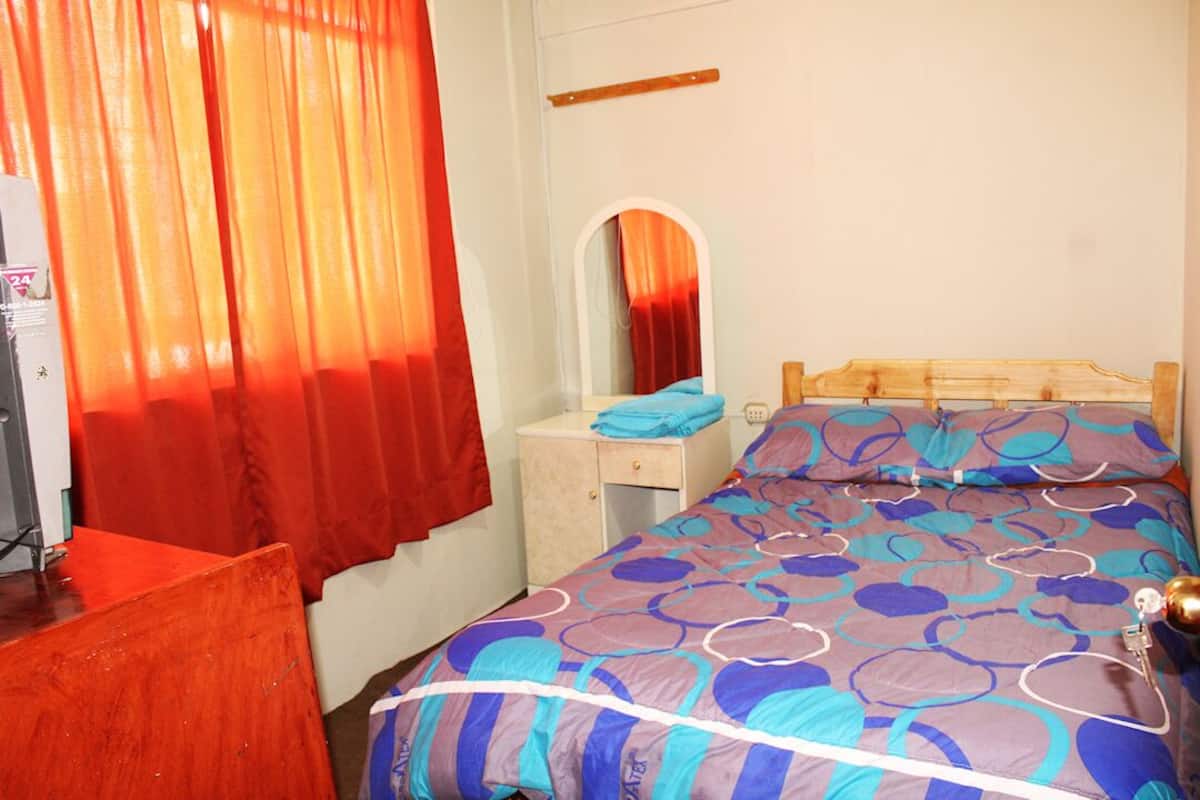 A bedroom with a bed, a nightstand, a mirror, and a desk with a chair.