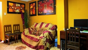 A living room with a yellow wall, a couch, two chairs, a TV, and artwork. - Hostel Climbing Point (Independencia)