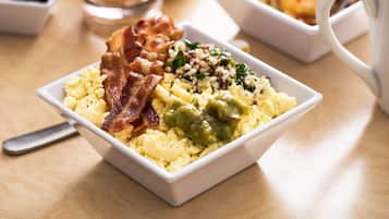 Une assiette de petit-déjeuner avec des œufs brouillés, du bacon et une sauce verte.