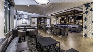 Um lobby de hotel moderno com área de bar, espaços para sentar e uma grande janela com vista.