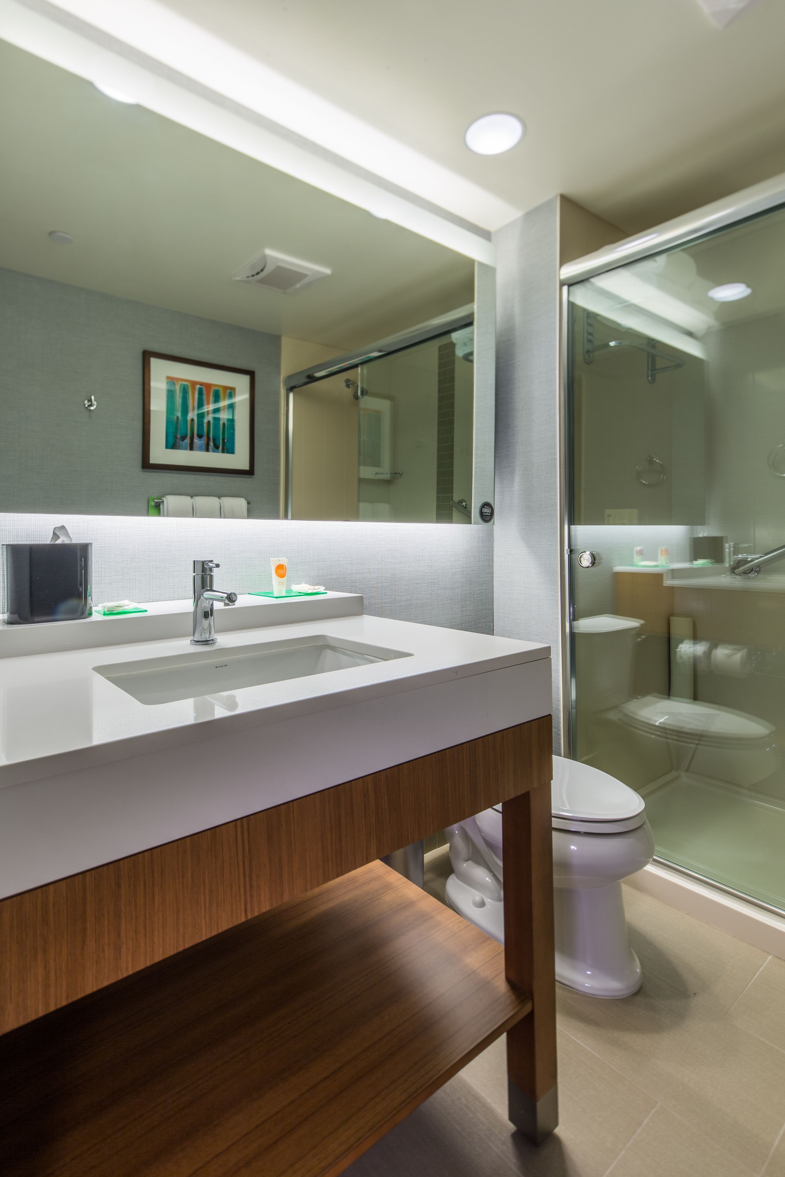 Un baño moderno con lavamanos blanco, espejo y cabina de ducha con mampara de vidrio.