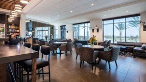 Um lobby moderno de hotel com área de bar, espaços de estar e grandes janelas com vista.