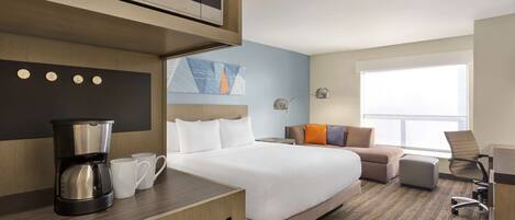 Habitación de hotel con cama, escritorio con cafetera, silla y ventana grande.
