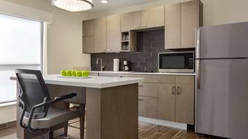 Una cocina moderna con armarios de madera, un refrigerador de acero inoxidable, un microondas y una barra con una silla y manzanas verdes.