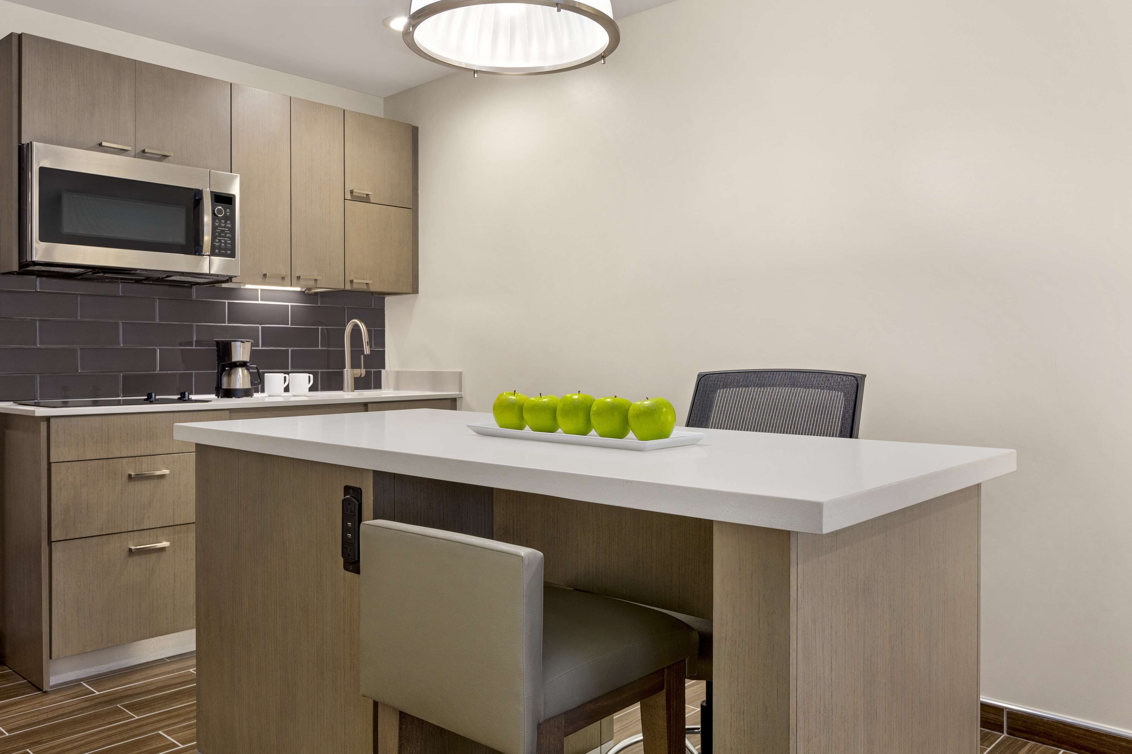 A modern kitchen with a built-in microwave, a coffee maker, and a plate of green apples on the counter.