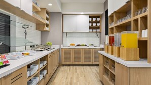 A modern kitchen with wooden cabinets, a white countertop, and various food items displayed. - Hyatt House Bryan/College Station (Bryan)