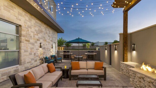 An outdoor patio with a stone wall, a fire feature, and string lights. - Hyatt House Bryan/College Station (Bryan)