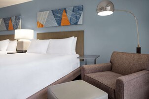 Habitación de hotel con una cama grande, una mesita de noche, una lámpara, una silla y una pequeña mesa.