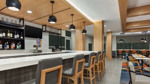 A modern bar area with a long counter, bar stools, and a variety of liquor bottles. - Hyatt House Bryan/College Station (Bryan)