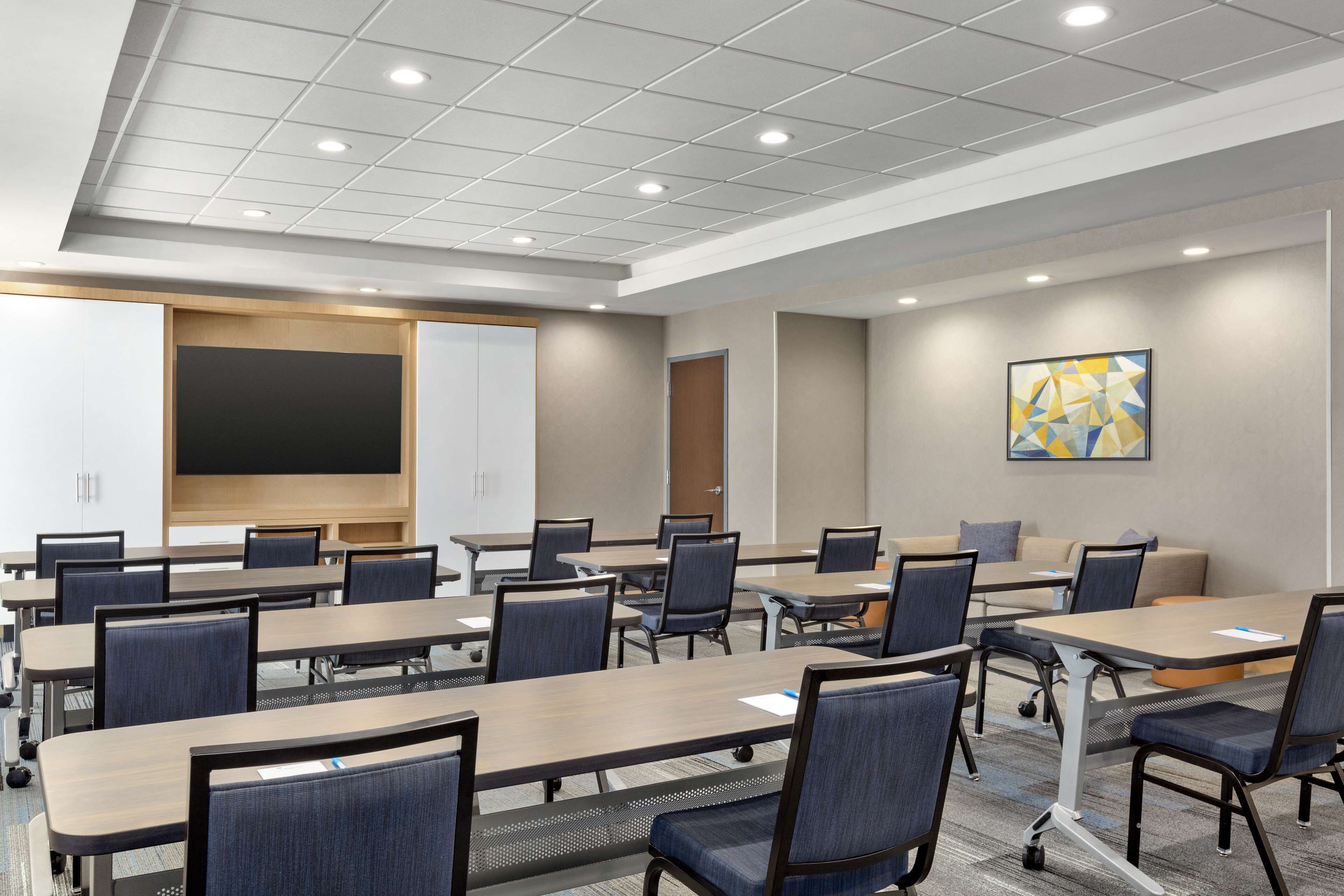 A conference room with multiple tables and chairs, a large screen, and a door.