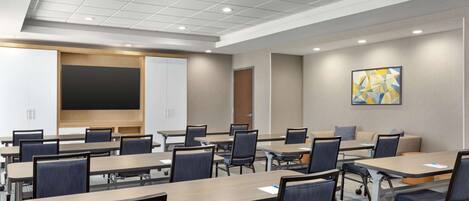 A conference room with multiple tables and chairs, a large screen, and a door.