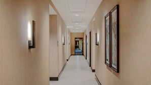 Un couloir d’hôtel avec des œuvres d’art encadrées accrochées aux murs, un éclairage encastré et un sol carrelé.