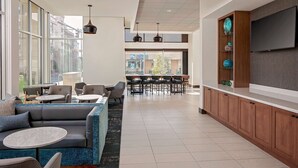 Un hall d’hôtel moderne doté d’un espace salon, d’un bar et de grandes fenêtres offrant une vue sur la ville.