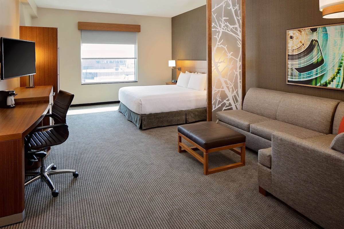 Une chambre d’hôtel comprenant un lit, un canapé, un bureau avec une chaise, une télévision et une fenêtre donnant sur des immeubles.