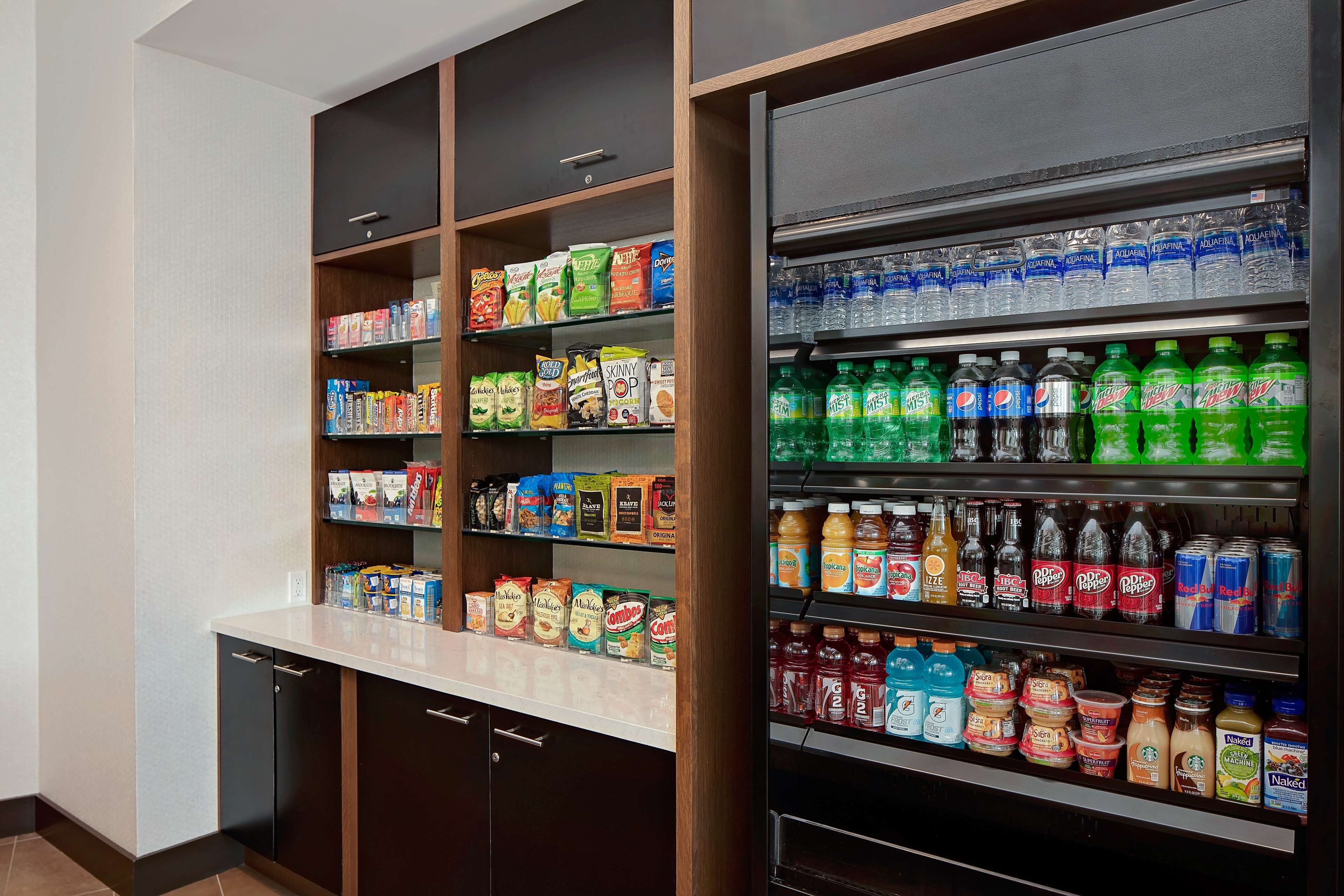Una kitchenette con un refrigerador lleno de bebidas y una despensa con aperitivos y condimentos.