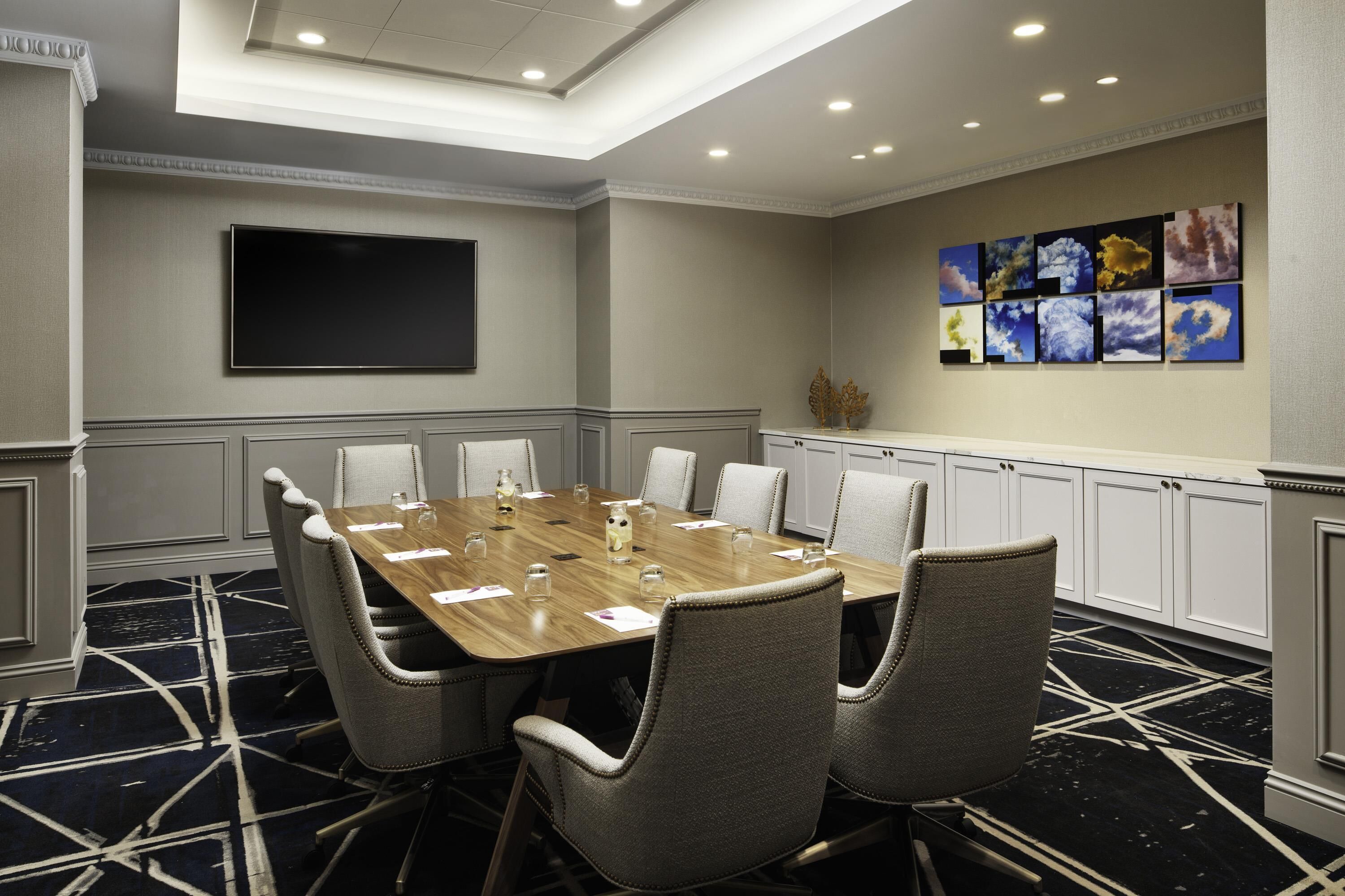 Un salón de conferencias con una larga mesa, seis sillas, un televisor de pantalla plana y una pared con cuadros enmarcados.