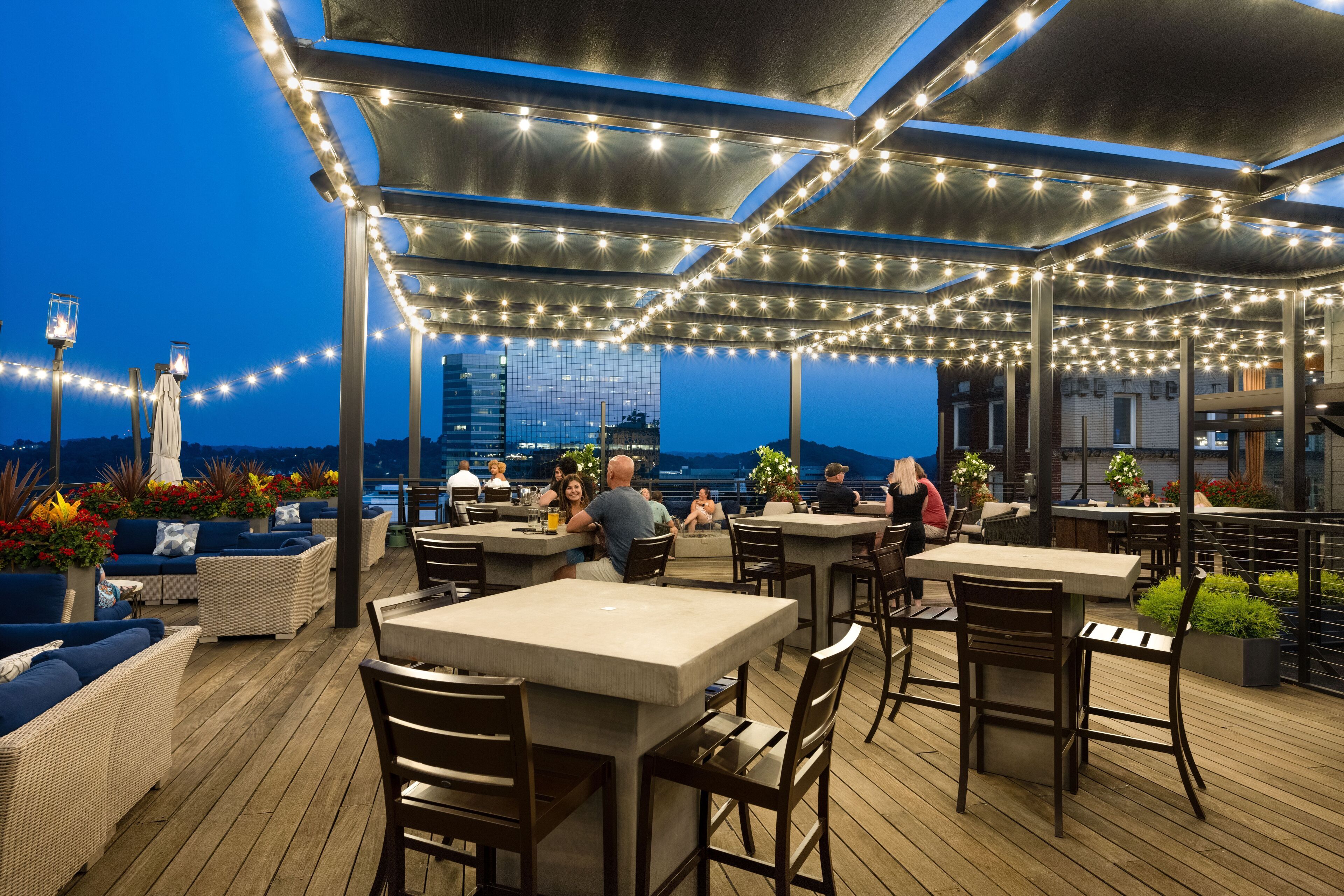 An outdoor dining area with tables and chairs, string lights, and potted plants.