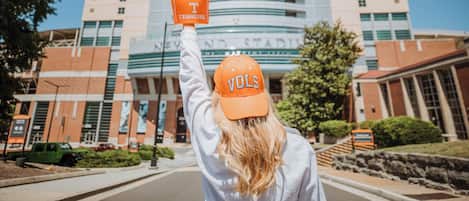 A person wearing a cap and glove with "VOL" and "Tennessee" visible, standing in front of a building with "STADY" on the facade.