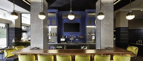 Una zona de bar con una larga barra de madera, varias sillas amarillas y lámparas colgantes.
