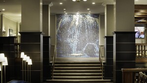 A grand staircase with a decorative wall at the top, flanked by tall columns and modern lighting fixtures. - Hyatt Place Knoxville Downtown (Knoxville)