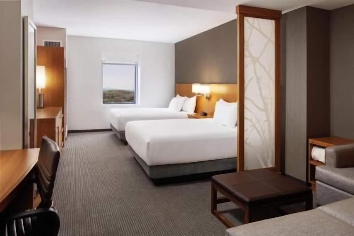 A hotel room with two beds, a desk, a chair, a small table, and a view of the outdoors.